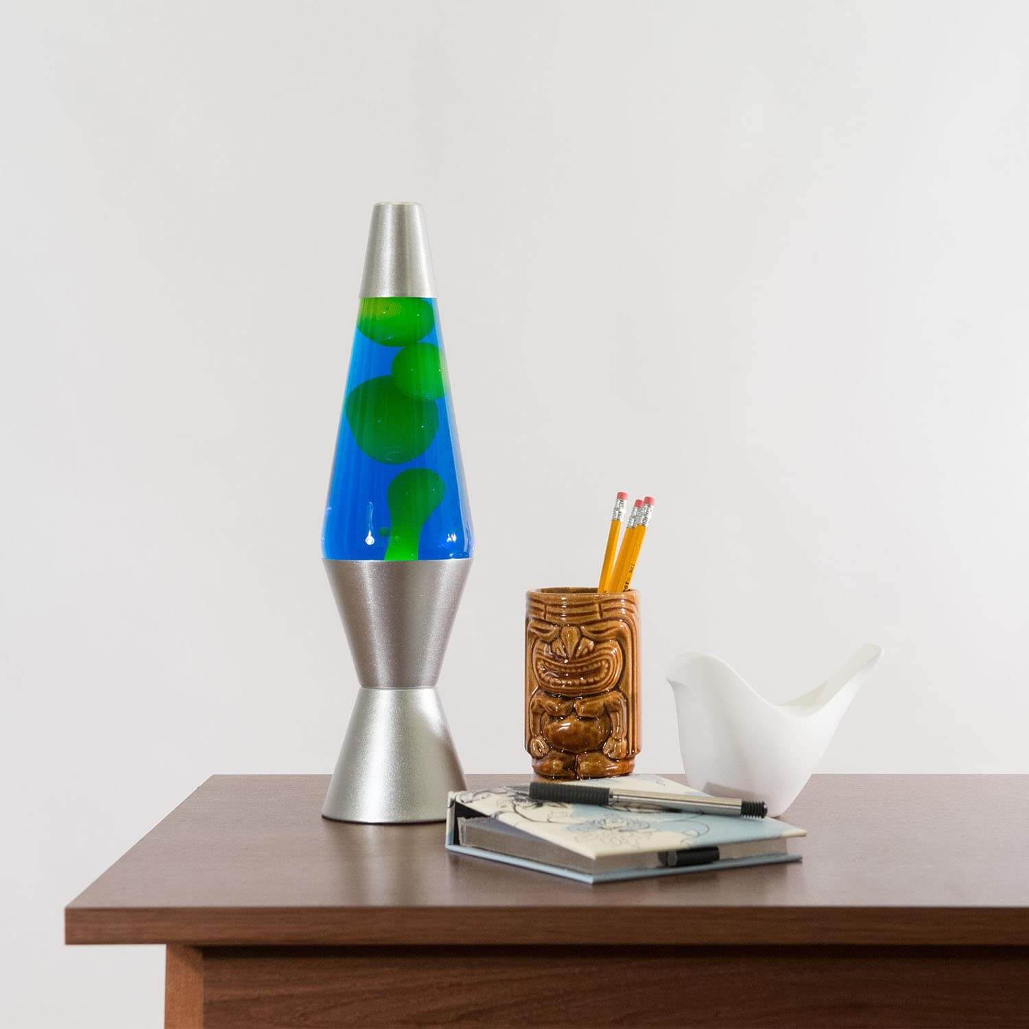 Blue and green lava lamp placed on a wooden table next to a drink and glasses, adding a retro touch to minimalist home decor