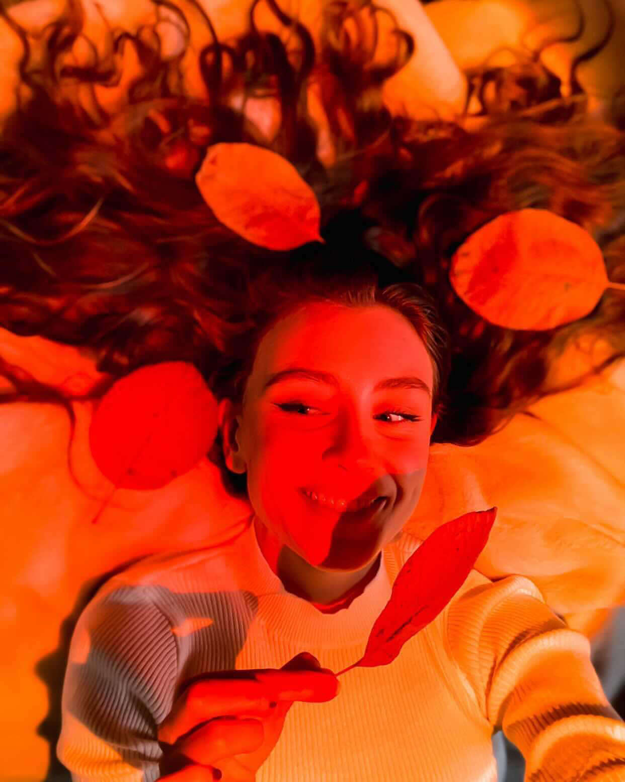Person lying on a bed with a warm orange glow from a sunset lamp, surrounded by soft pillows and bathed in cozy ambient lighting.