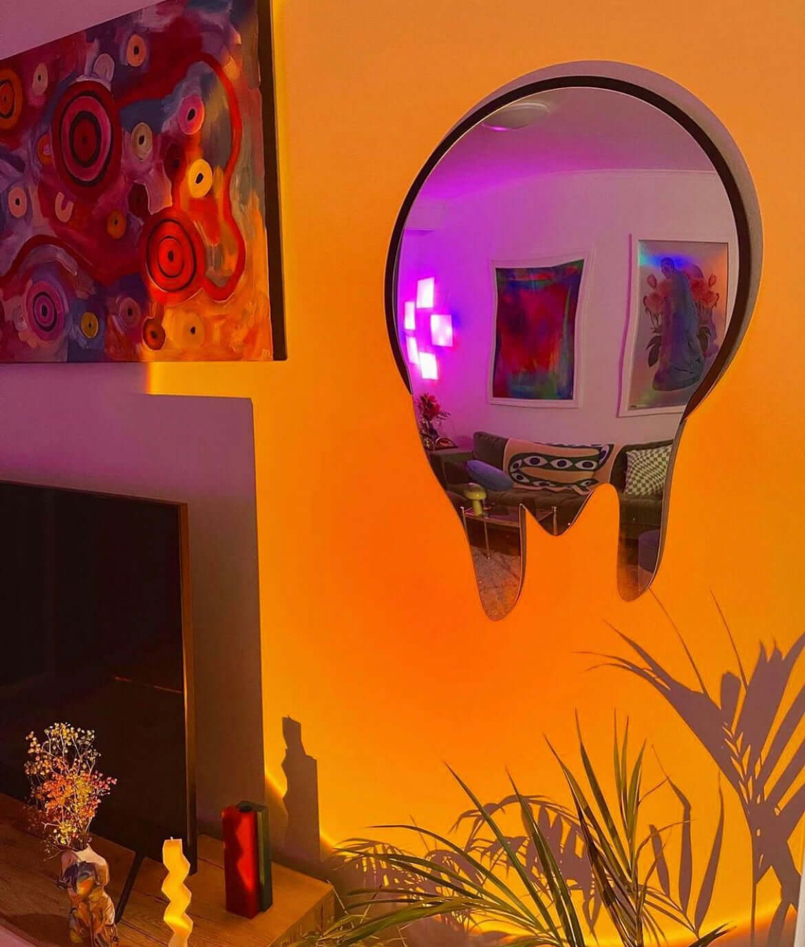 Sunset lamp casting a warm orange glow on a decorated wall with a round mirror reflecting purple light, creating a cozy and artistic room ambiance.