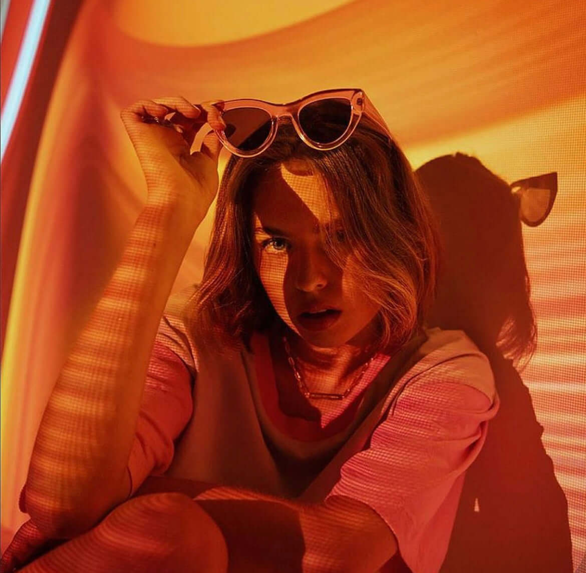 Young woman sitting in a softly lit room with a sunset lamp casting warm orange tones, creating a cozy and relaxed atmosphere.
